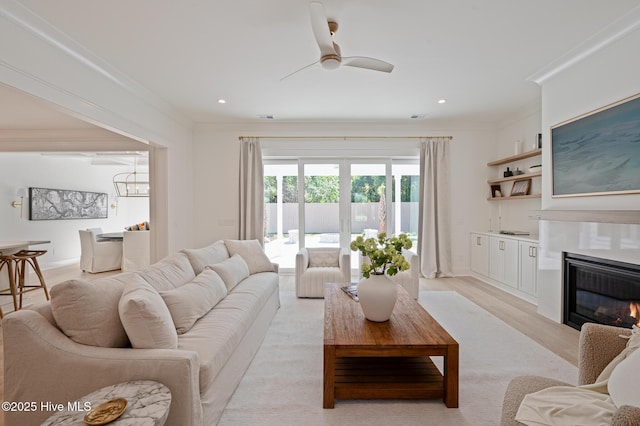 living area with ornamental molding, a ceiling fan, a glass covered fireplace, recessed lighting, and light wood finished floors