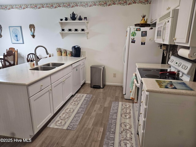 kitchen featuring white appliances, a sink, a peninsula, light wood-style flooring, and light countertops