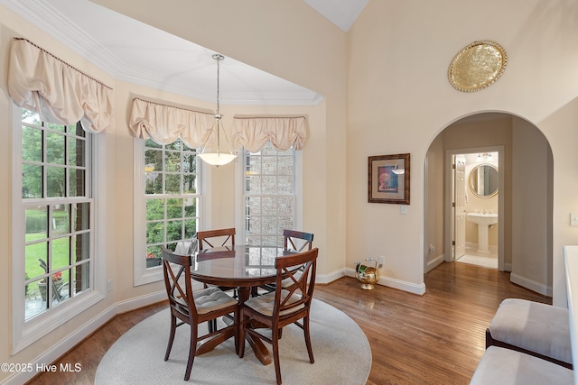 dining space featuring arched walkways, wood finished floors, baseboards, and crown molding