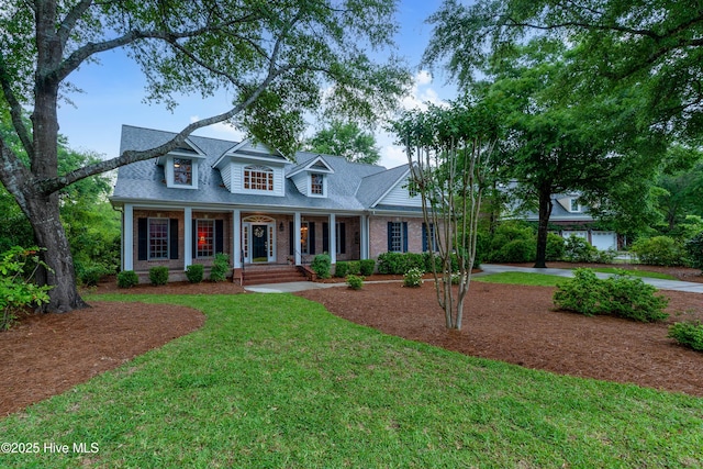 cape cod home with covered porch, brick siding, a front lawn, and roof with shingles