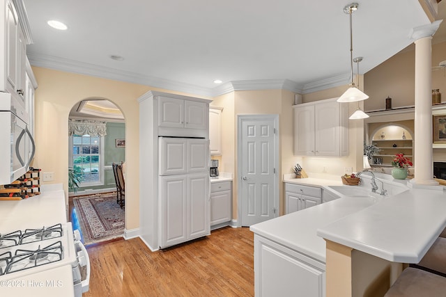 kitchen with a sink, arched walkways, white appliances, a kitchen bar, and light wood-type flooring