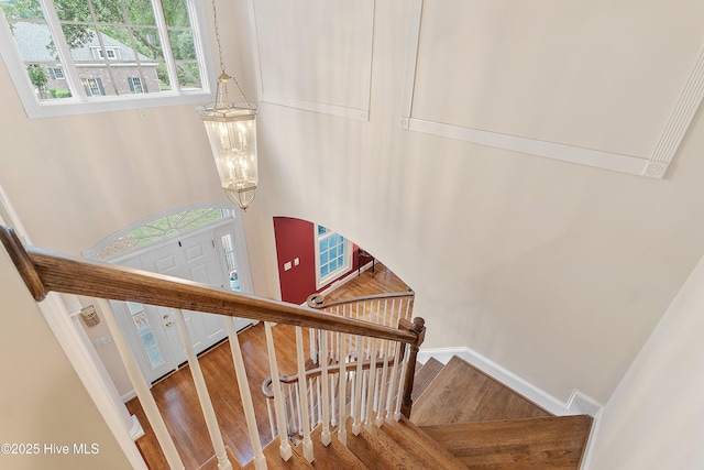 stairway with wood finished floors, healthy amount of natural light, and a chandelier