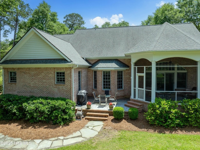 back of house featuring a patio area, roof with shingles, brick siding, and a sunroom