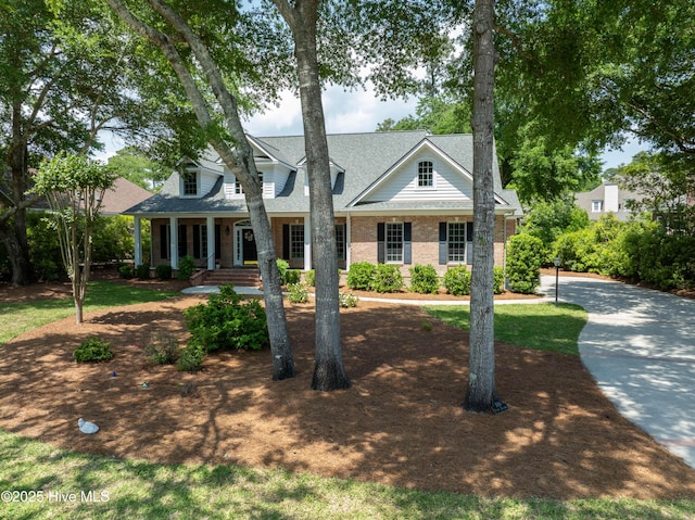 cape cod home with a shingled roof, brick siding, and a porch