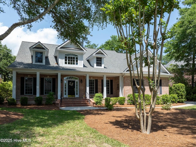 view of front facade with brick siding, roof with shingles, a porch, and a front yard