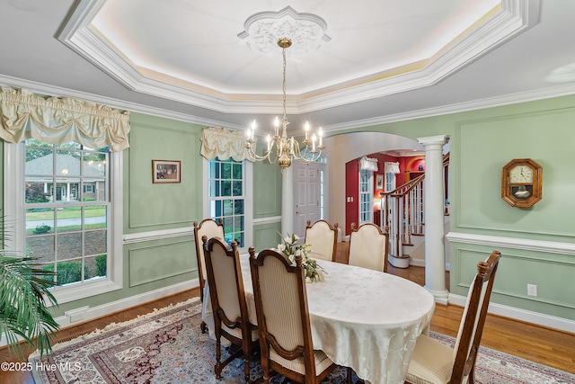 dining room featuring a raised ceiling, arched walkways, plenty of natural light, decorative columns, and crown molding