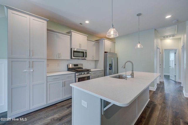 kitchen with a sink, appliances with stainless steel finishes, a center island with sink, dark wood-type flooring, and backsplash