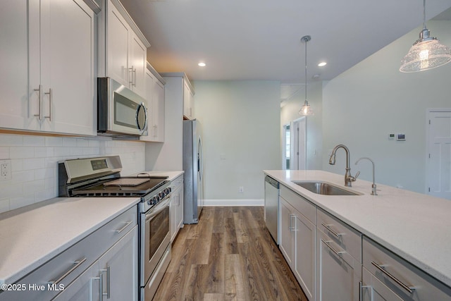 kitchen featuring stainless steel appliances, a sink, dark wood-style flooring, light countertops, and decorative backsplash