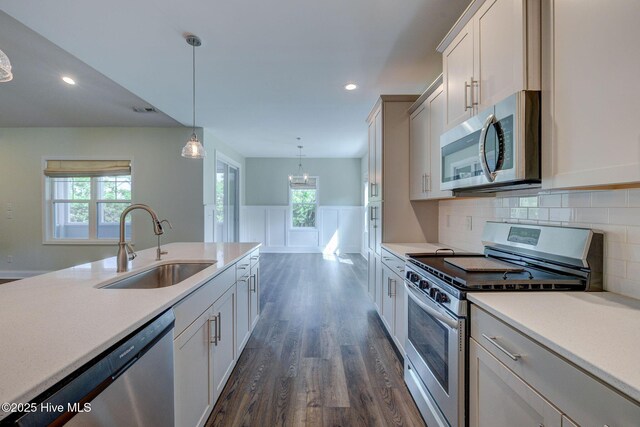 kitchen featuring appliances with stainless steel finishes, a sink, dark wood-style floors, light countertops, and wainscoting