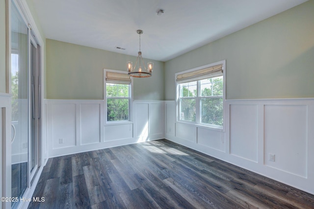 unfurnished dining area featuring a wainscoted wall, a decorative wall, a chandelier, and dark wood finished floors