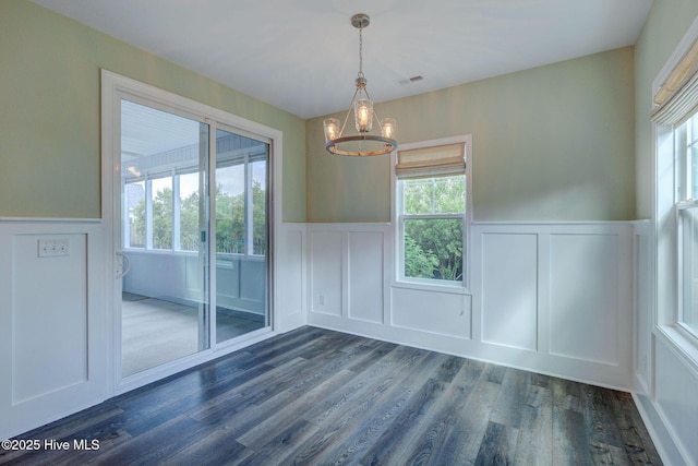 unfurnished dining area with a decorative wall, a wainscoted wall, a chandelier, dark wood finished floors, and healthy amount of natural light