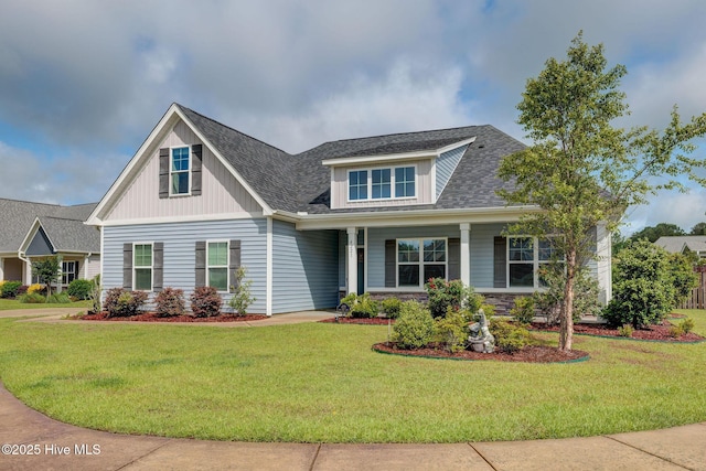 craftsman-style home with a front yard, a shingled roof, stone siding, and a porch