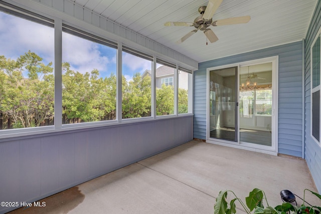 unfurnished sunroom with ceiling fan, a chandelier, and wood walls