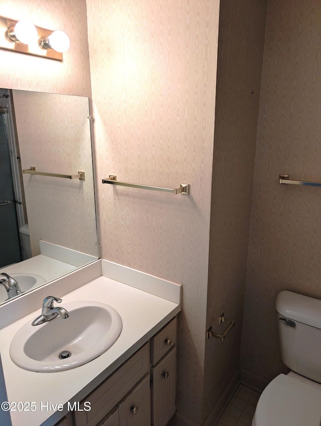 bathroom with toilet, wallpapered walls, vanity, and tile patterned floors