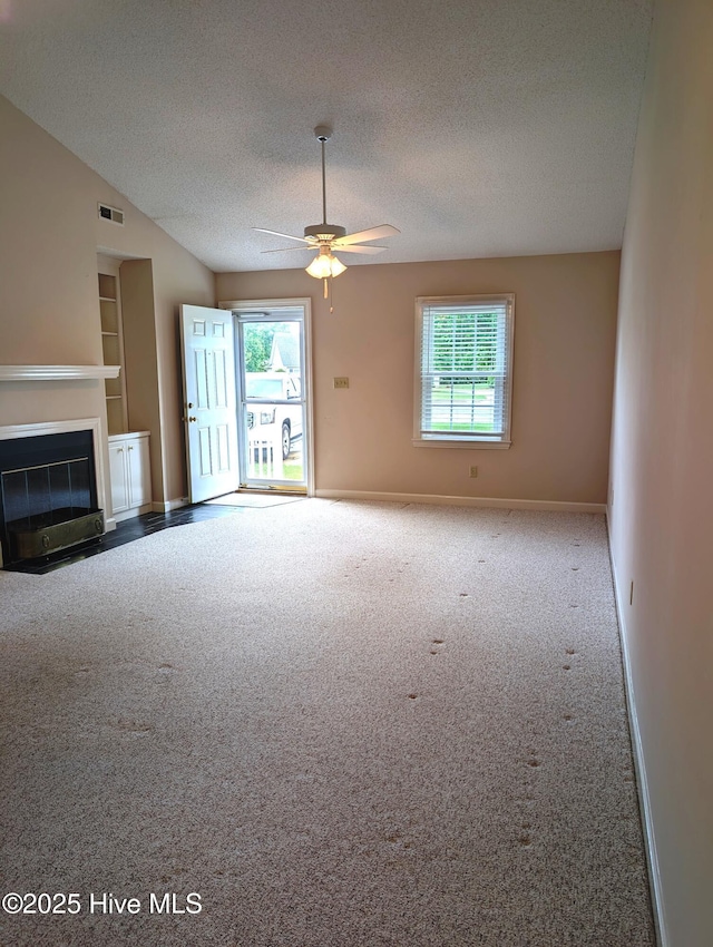unfurnished living room featuring plenty of natural light, a textured ceiling, carpet flooring, a ceiling fan, and a fireplace with flush hearth