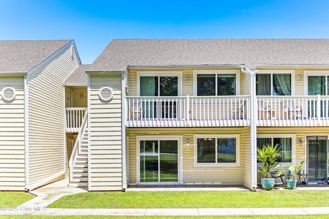rear view of house with a balcony, roof with shingles, and a yard
