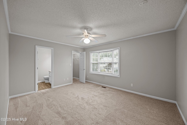unfurnished bedroom featuring ornamental molding, carpet, a textured ceiling, ensuite bathroom, and baseboards