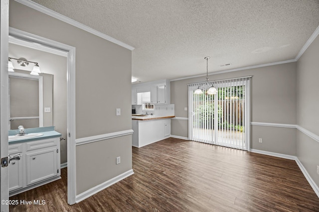 unfurnished dining area featuring a textured ceiling, a sink, dark wood-style floors, ornamental molding, and baseboards