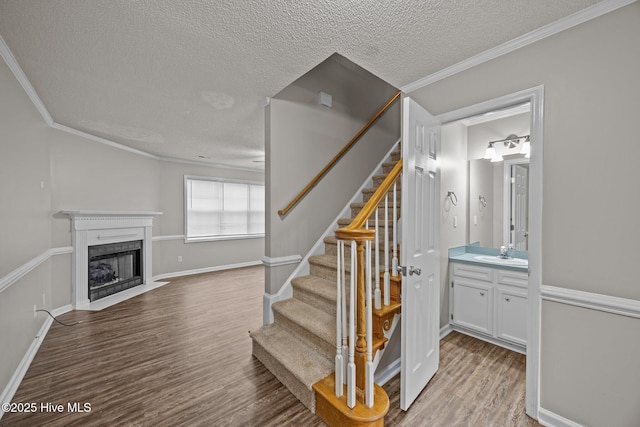 staircase featuring a textured ceiling, wood finished floors, ornamental molding, a fireplace with flush hearth, and baseboards
