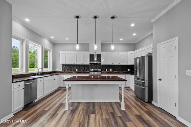 kitchen featuring stainless steel appliances, wall chimney range hood, a sink, dark wood finished floors, and ornamental molding