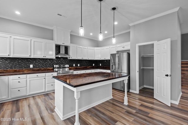 kitchen featuring wooden counters, stainless steel appliances, wall chimney exhaust hood, crown molding, and white cabinetry