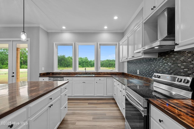 kitchen featuring stainless steel range with electric cooktop, wall chimney range hood, a sink, butcher block countertops, and plenty of natural light