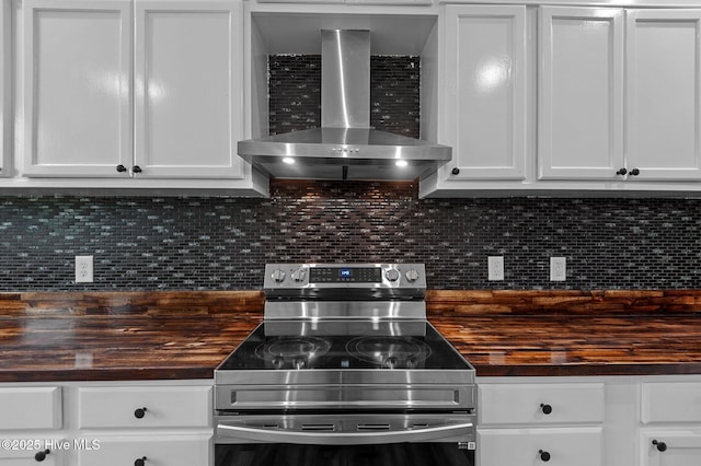kitchen with stainless steel range with electric stovetop, wood counters, wall chimney range hood, decorative backsplash, and white cabinets