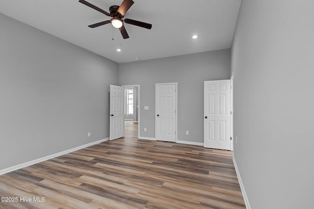 unfurnished bedroom featuring baseboards, wood finished floors, recessed lighting, a towering ceiling, and ceiling fan