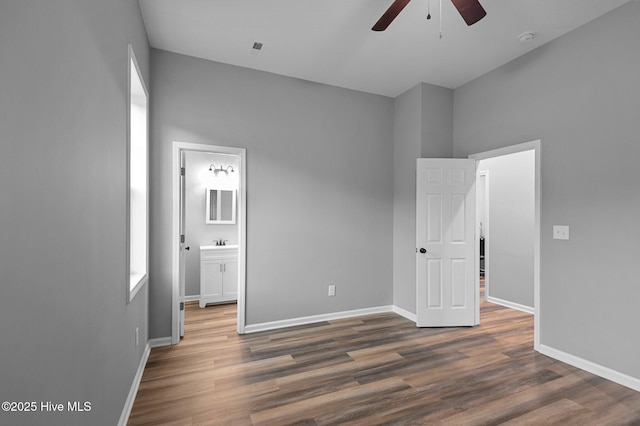 unfurnished bedroom featuring wood finished floors, baseboards, connected bathroom, and a ceiling fan