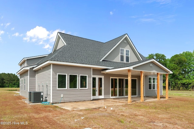 rear view of property with a patio, central AC, roof with shingles, and a lawn