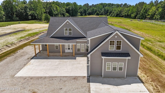 view of front facade featuring driveway, a shingled roof, a view of trees, and a front lawn