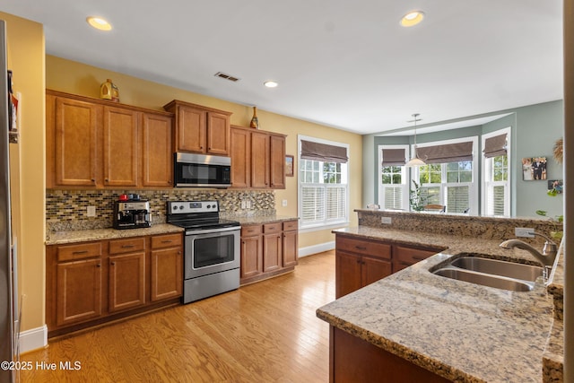 5613 Swiss Stone Ct, Wilmington, NC 28412 - kitchen with stainless steel appliances, a sink, brown cabinetry, light wood-type flooring, and backsplash