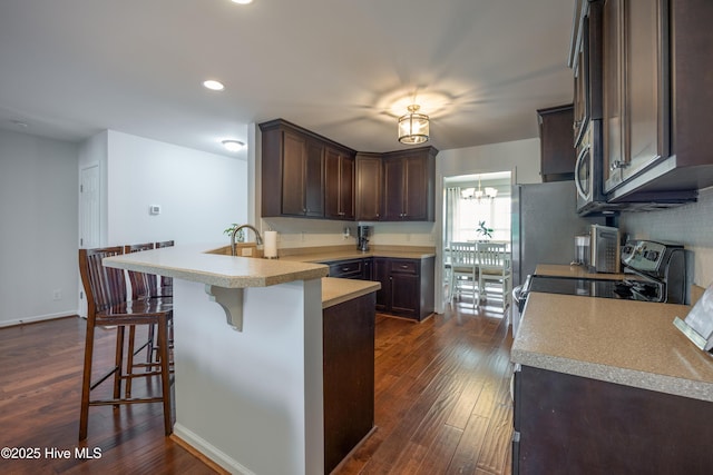 104 Northgate Ln, Clinton, NC 28328 - kitchen with a peninsula, dark brown cabinets, dark wood finished floors, a kitchen bar, and light countertops