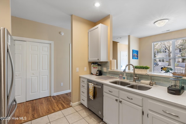 kitchen with appliances with stainless steel finishes, a sink, light countertops, backsplash, and white cabinets