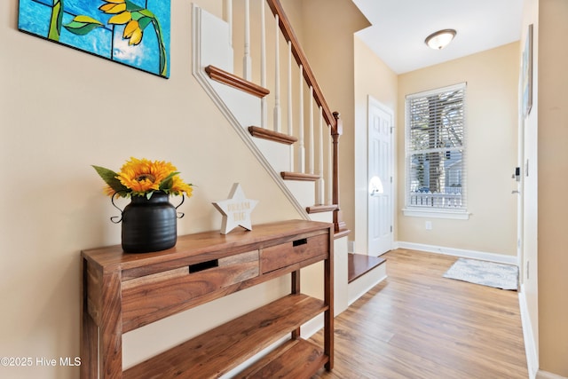 foyer entrance with light wood-type flooring, baseboards, and stairway
