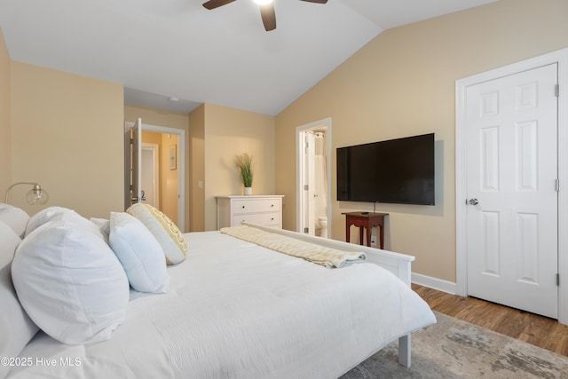 bedroom featuring wood finished floors, lofted ceiling, baseboards, ensuite bath, and a ceiling fan