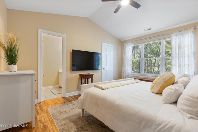 bedroom featuring vaulted ceiling, light wood finished floors, ensuite bath, a ceiling fan, and baseboards