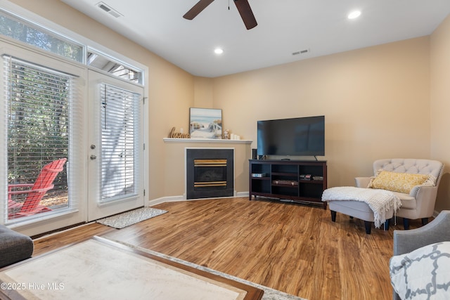 living area with wood finished floors, a ceiling fan, a glass covered fireplace, recessed lighting, and baseboards