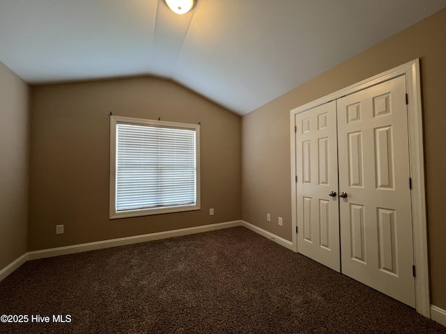 unfurnished bedroom featuring vaulted ceiling, dark colored carpet, a closet, and baseboards