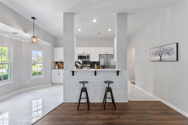kitchen with stainless steel appliances, a kitchen bar, baseboards, light countertops, and white cabinets