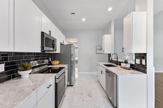 kitchen with stainless steel appliances, a sink, light marble finish floors, baseboards, and recessed lighting