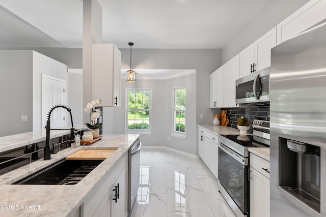 kitchen featuring appliances with stainless steel finishes, a sink, light marble finish floors, baseboards, and tasteful backsplash