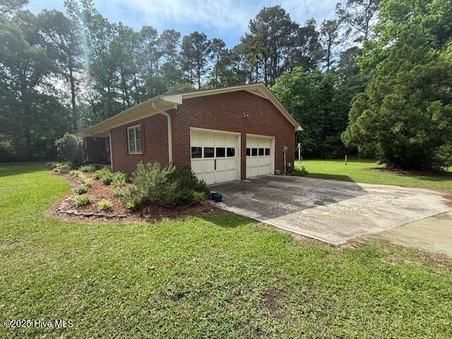 view of home's exterior with concrete driveway, brick siding, a lawn, and an attached garage