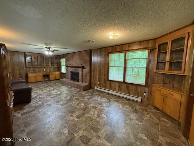 unfurnished living room featuring baseboard heating, wood walls, healthy amount of natural light, a ceiling fan, and a fireplace