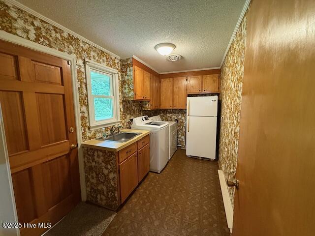 kitchen with freestanding refrigerator, a sink, wallpapered walls, ornamental molding, and brown cabinetry