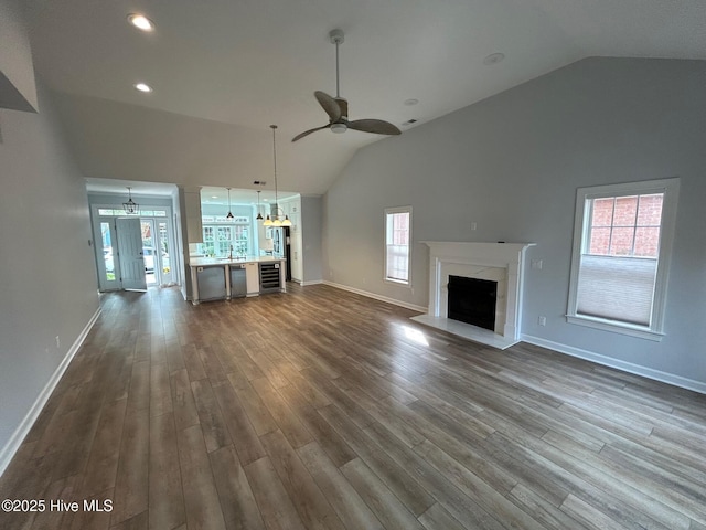 unfurnished living room with ceiling fan, lofted ceiling, a high end fireplace, plenty of natural light, and dark wood-type flooring