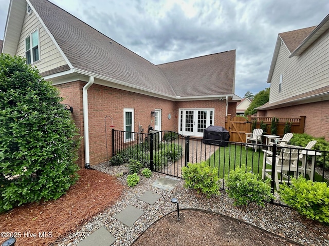 back of property featuring fence, brick siding, and roof with shingles