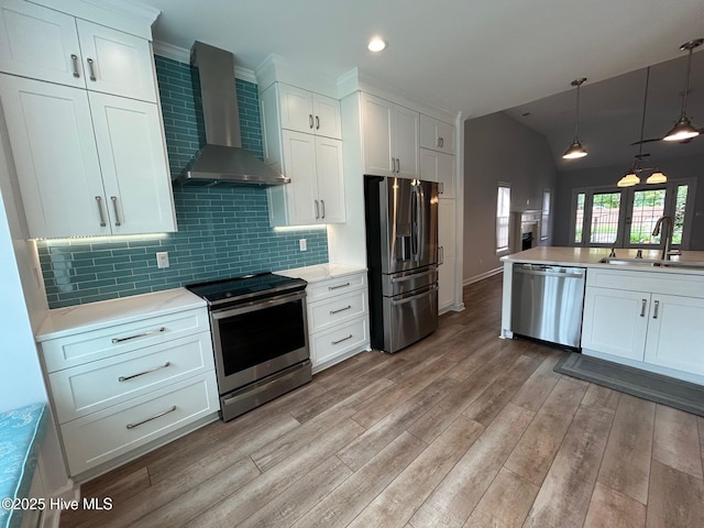 kitchen with stainless steel appliances, wall chimney range hood, a sink, light countertops, and light wood-style floors