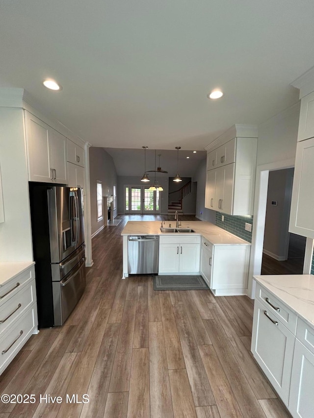 kitchen with appliances with stainless steel finishes, a sink, a peninsula, white cabinets, and wood finished floors