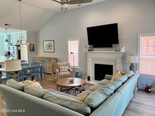 living room featuring a ceiling fan, vaulted ceiling, light wood-style floors, a high end fireplace, and baseboards